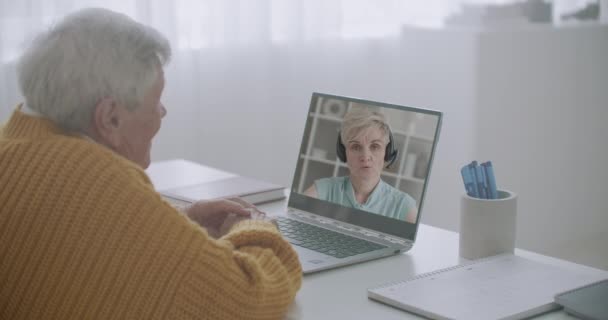 Homem idoso está conversando com sua filha adulta por videochamada no notebook de casa, mulher está falando, seu rosto em exposição — Vídeo de Stock