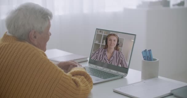 Starý muž se dívá na obrazovku notebooku a poslouchá svou vnučku, chatuje s příbuznými vzdáleně přes internet, vzdálená komunikace — Stock video