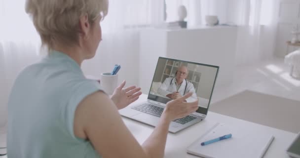 Frau ruft Arzt per Videokonferenz von zu Hause an, gealterte, erfahrene Medizinprofessorin beantwortet ihre Fragen — Stockvideo