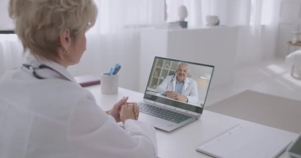 Dois especialistas médicos experientes estão trocando conhecimento e experiência, conversando on-line por videochamada no notebook — Vídeo de Stock