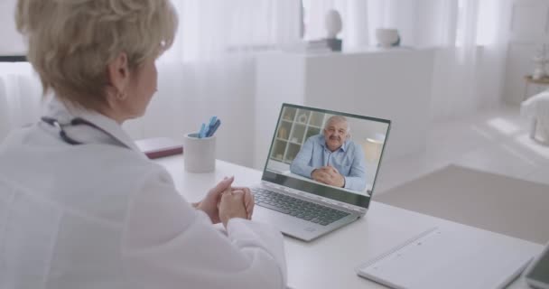 Médico de familia está hablando con el paciente masculino por ordenador portátil, mediante videollamada, el hombre está hablando de su salud y enfermedad — Vídeo de stock