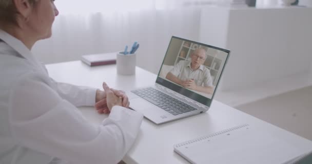 Sick aged man is calling his doctor and talking about symptoms of his illness, using video chat at laptop, woman physician is listening to him — Stock Video