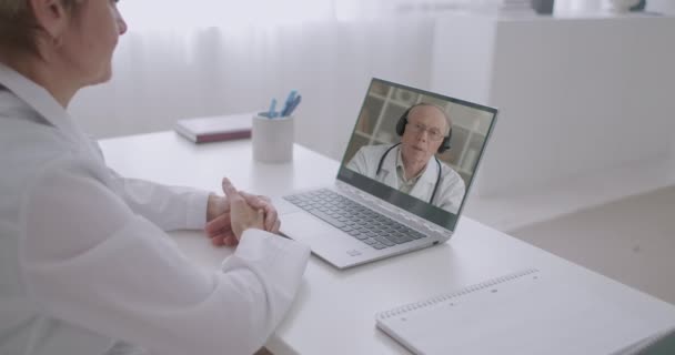 Ve věku zkušený lékař konzultuje ženskou terapeut nemocnice videohovory, žena sedí ve své kanceláři a prohlížení na obrazovce notebooku — Stock video