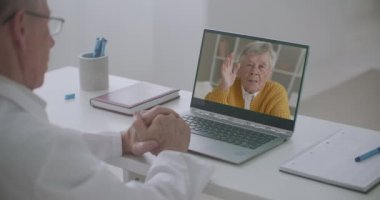 Yaşlı bir adam aile doktorunu telefonla arıyor, konuşuyor ve ona danışıyor. Doktor dizüstü bilgisayarın görüntüsüne bakıyor.
