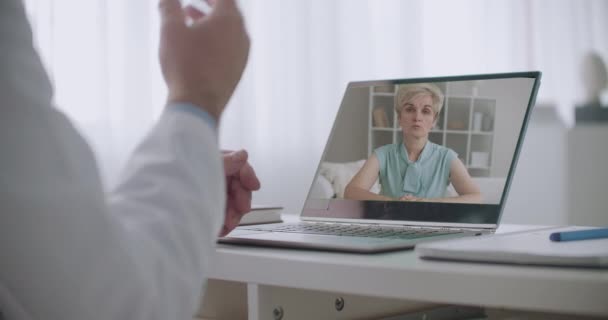 Paziente adulto e terapeuta stanno discutendo tramite videochiamata, faccia paziente in mostra del computer portatile, primo piano delle mani dei medici — Video Stock