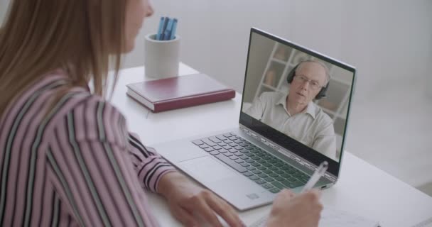 Studente sta prendendo appunti di lezione online del professore universitario, comunicare con lui tramite videochiamate, utilizzando il computer portatile — Video Stock