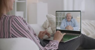 Evde video sohbetiyle öğrenim gören kız öğrenci, dizüstü bilgisayar ekranında orta yaşlı erkek öğretmenin konferansını dinliyor