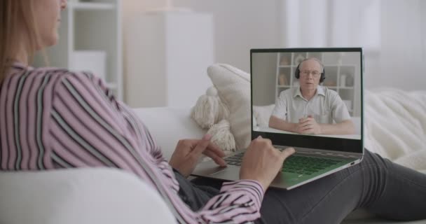 Jonge vrouw communiceert met oudere mannelijke psycholoog via videogesprek, scherm van laptop bekijken, thuisblijven — Stockvideo
