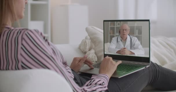 Starší lékař přednáší on-line pro pacienty, mladá žena prohlíží video notebookem doma, konzultace a zdravotní péče — Stock video