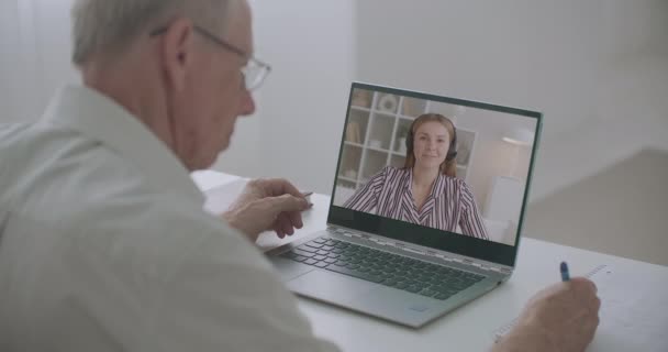 Mensen werken op afstand, communiceren via videogesprekken, oude man maakt aantekeningen en jonge vrouw praat. — Stockvideo