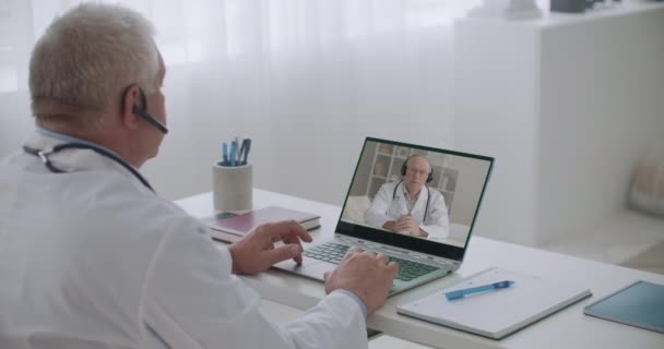 Terapeuta está escuchando médico jefe por servicio de videoconferencia, hombre mayor en la pantalla está hablando y dando órdenes — Vídeos de Stock