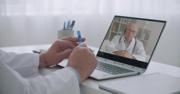 Dois terapeutas estão consultando on-line uns aos outros por videoconferência de seus escritórios em clínicas, médico idoso na tela está ouvindo — Vídeo de Stock