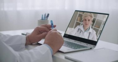 Kadın doktor, iş arkadaşına internet üzerinden danışmanlık yapıyor. Doktor, ofisteki dizüstü bilgisayardan yüzünü izliyor.