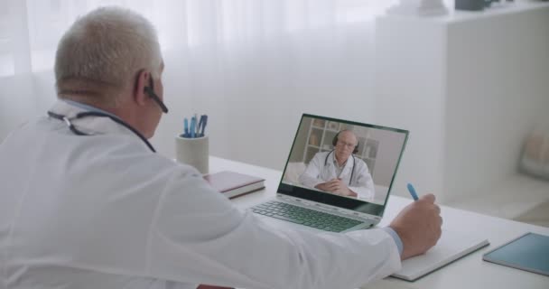 Överläkare pratar med läkare på sjukhus på nätet, videokonferens på morgonen, manlig terapeut lyssnar och antecknar — Stockvideo