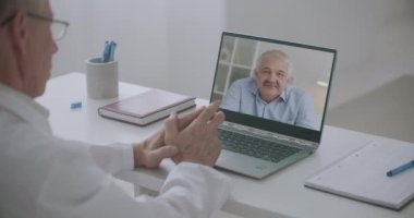 Hekim orta yaşlı erkek hastayı dinliyor. Laptop ekranına bakıyor. Tecrit sürecinde uzaktan tıbbi konsültasyon.