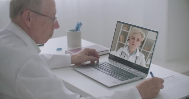 Médico jefe está escuchando informe de médico femenino por videollamada, viendo su cara en la pantalla de la computadora portátil — Vídeo de stock