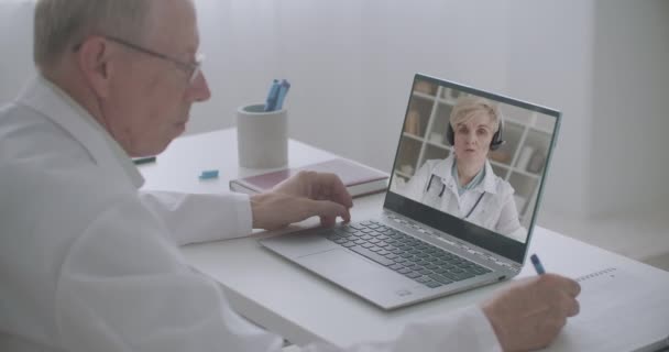 Conferência on-line de profissionais de saúde, o homem está tomando notas de palestra de médico do sexo feminino, visualização no notebook — Vídeo de Stock