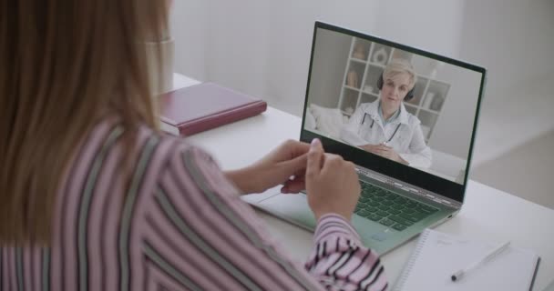 Jonge moeder is overleg met vrouwelijke kinderarts via internet, bellen door webcamera op laptop, thuisblijven — Stockvideo