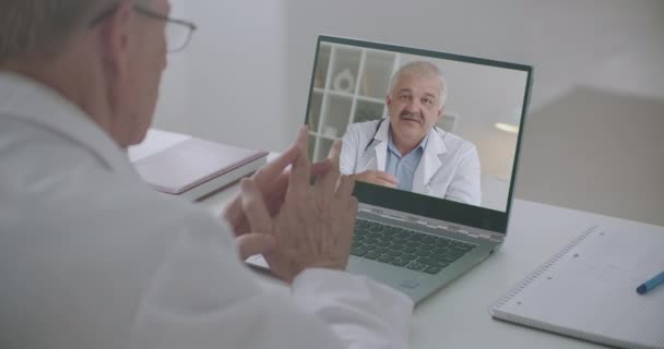 Dos médicos de medicina se está comunicando por videollamada en el ordenador portátil, consultando y discutiendo a distancia — Vídeo de stock