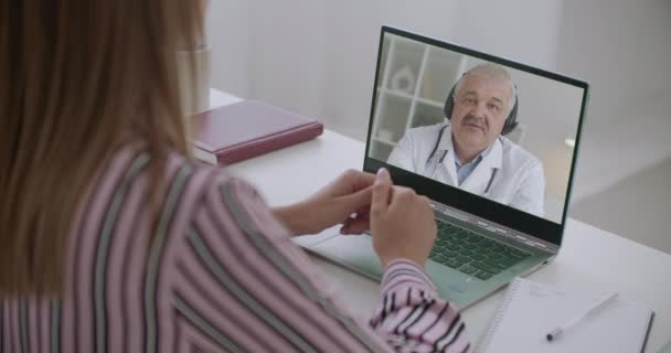 Dokter paruh baya berbicara dengan pasien wanita melalui panggilan video di laptop, wanita mendengarkan spesialis medis duduk di rumah — Stok Video