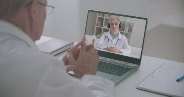 インターネットによる医師のオンライン会議では男性と女性がノートパソコンのウェブカメラでコミュニケーションをとり議論しています — ストック動画