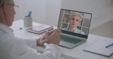 Yaşlı bir kadın doktorla web kamerasıyla iletişim kuruyor. Yüzü doktor dizüstü bilgisayarında. Teletıp seansı.