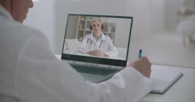 Kadın doktor not defterine video konferansı veriyor, erkek arkadaşı da dinliyor ve notlar yazıyor.