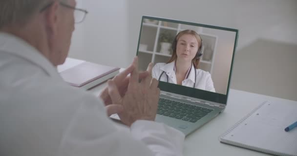Jonge vrouwelijke gezondheidswerker is overleg met ervaren arts via online chat met behulp van notebook — Stockvideo