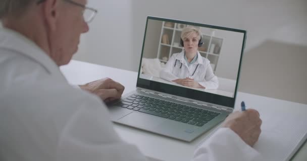 Doctora de medicina está dando conferencias en línea, terapeuta masculino está escuchando y escribiendo, viendo por ordenador portátil — Vídeo de stock