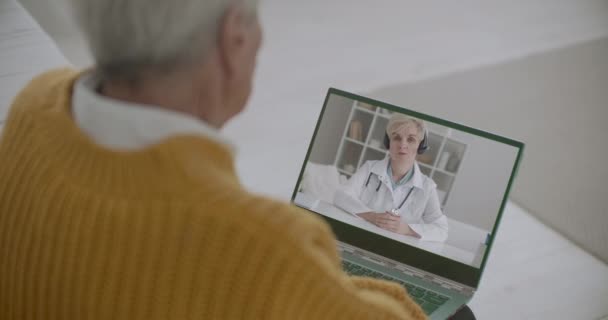Terapeuta está falando sobre nova infecção por coronavírus e medidas preventivas ao paciente idoso por videochamada, homem está listando por laptop — Vídeo de Stock