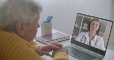 Genç bayan doktor yaşlı adama video görüşmesiyle danışmanlık yapıyor, kıdemli kişi de dinliyor ve not defterindeki doktoru izliyor.