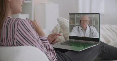 Kadın doktorla video konuşarak sağlığından bahsediyor, evde oturuyor, yaşlı tıp profesörü onu dinliyor.