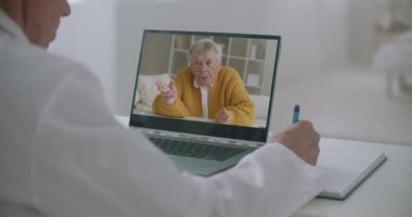 Yaşlı hasta, doktorla semptomlar ve hastalıklar hakkında konuşuyor. Video çağrısı, ofisteki hekimlerin dizüstü bilgisayarındaki yüzü.