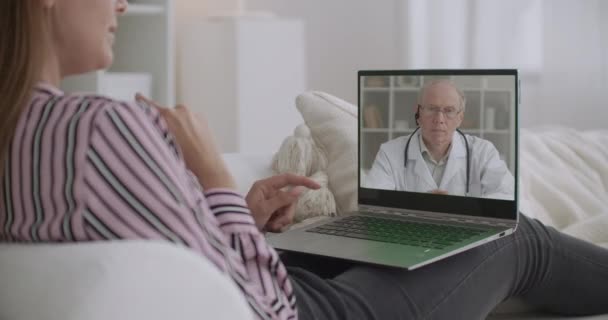 Mulher está conversando com o médico sobre sua saúde por videochamada, sentado em casa, professor de medicina idoso está ouvindo ela — Vídeo de Stock