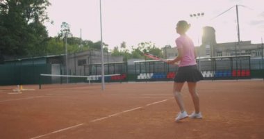 Sahada tenis oynayan, ağır çekimde topu geri getiren beyaz bir kadının yan görüntüsü.