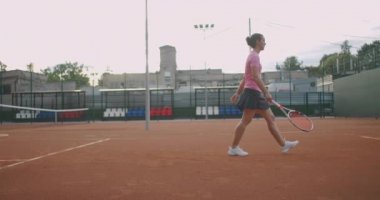 Çekici sporcu tenis kortunda ağ yakınında poz veriyor. Genç atletik bayan tenis oynuyor, kapalı sahada yürüyor, kadın oyuncu oyun pozisyonu alıyor, antrenman günü