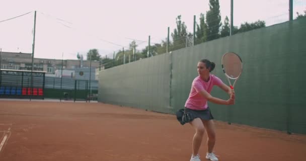 Joven mujer caucásica jugando al tenis en una cancha, devolviendo una pelota en cámara lenta — Vídeos de Stock