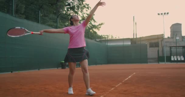 Visão lateral em câmera lenta de um jovem atleta treina o serviço da bola de tênis. Um atleta adolescente está jogando tênis em uma quadra. Uma garota ativa é poderosamente bater uma bola durante o esporte praticando — Vídeo de Stock