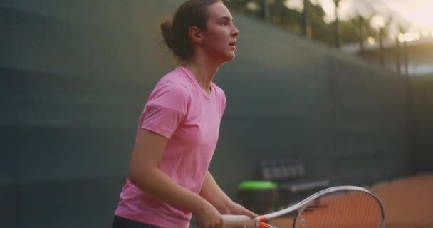 スローモーションテニスコートネットを通してテニス練習の商業映像。テニスをしている女性アスリートのストレートビュー。10代のスポーツマンがトレーニング中にボールを打つ — ストック動画
