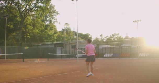 En trött brunett kvinnlig tennisspelare går längs tennisbanan återhämta sig och koncentrera sig. Bryt en tennismatch. Tennisspelare efter matchen på kartan vid solnedgången i slow motion. — Stockvideo