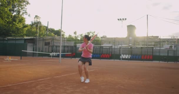 Mujer joven caminando por la cancha de tenis con raqueta. Vista trasera de atractiva morena femenina en camisa azul y pantalones cortos negros entrando en pista dura de tenis. Longitud completa seguir tiro con espacio de copia — Vídeos de Stock