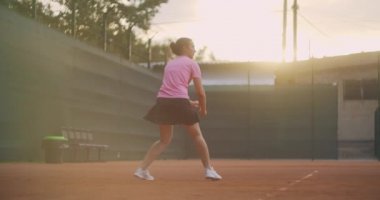Profesyonel donanımlı kadın tenis raketiyle tenis topuna sert vuruyor. Kadın tenisçi oyun sırasında iş başında. Üzerinde markasız spor giysiler var..