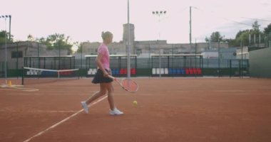 Çekici sporcu tenis kortunda ağ yakınında poz veriyor. Genç atletik bayan tenis oynuyor, kapalı sahada yürüyor, kadın oyuncu oyun pozisyonu alıyor, antrenman günü