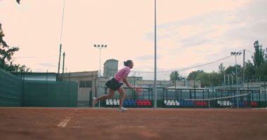 Tenis maçına hazırlanan genç bir bayan tenisçinin düşük açılı görüntüsü. Bir kadın atlet spor antrenmanı sırasında topa güçlü bir şekilde vuruyor. Ticari kullanım görüntüleri