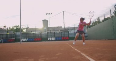 Slow Motion tenis kortu ağındaki tenis antrenmanının ticari görüntüleri. Tenis oynayan bir bayan sporcunun düz görüntüsü. Genç bir sporcu spor eğitiminde topa vuruyor.