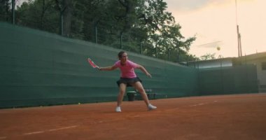Tenis maçına hazırlanan genç bir bayan tenisçinin düşük açılı görüntüsü. Bir kadın atlet spor antrenmanı sırasında topa güçlü bir şekilde vuruyor. Ticari kullanım görüntüleri