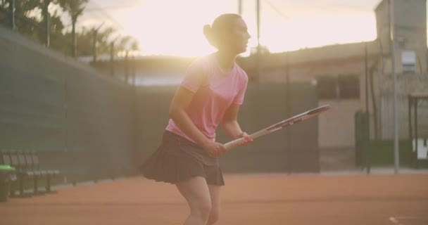 Filmagem comercial da prática de tênis através da rede de quadra de tênis. Vista directa de uma atleta a jogar ténis. Um esportista adolescente está batendo a bola durante o treinamento esportivo — Vídeo de Stock