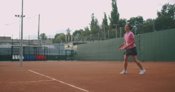 Jovem caucasiana jogando tênis em uma quadra, retornando uma bola em câmera lenta — Vídeo de Stock