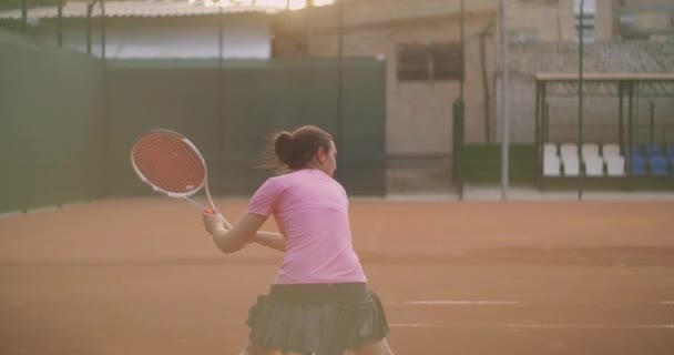 전문적 인 장비를 갖춘 여성이 테니스 라켓으로 테니스 공을 세게 때린다. 여자 테니스 선수는 경기중에 활동 한다. 이름도 모르는 운동복을 입고 있어요. — 비디오