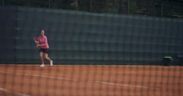 En ung brunett tennisspelare spelar en boll vid solnedgången på en tennisbana. En kvinna spelar tennis professionellt och dynamiskt i slow motion — Stockvideo